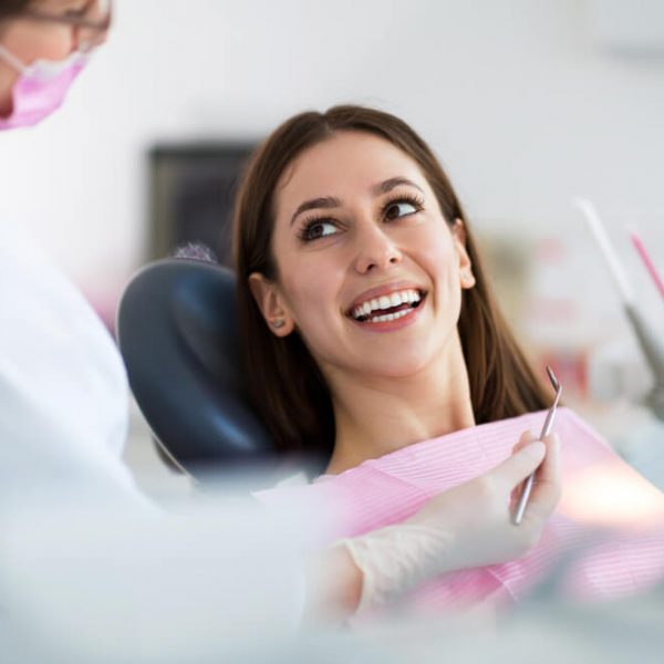 a young woman in the dental chair smiling and looking up at the dental hygienist