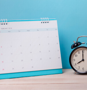 a calendar and an alarm clock on a desk with a blue background