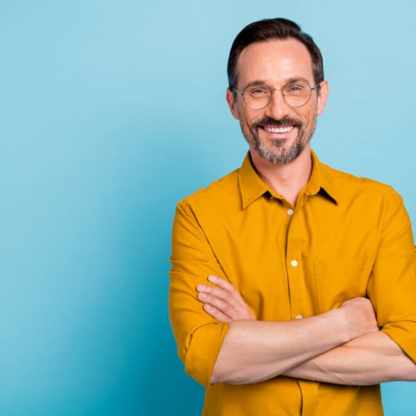 a middle aged man smiling with his arms crossed against a blue background