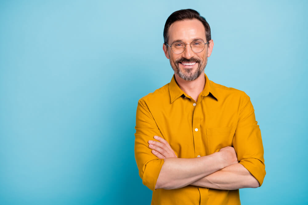 a middle aged man smiling with his arms crossed against a blue background