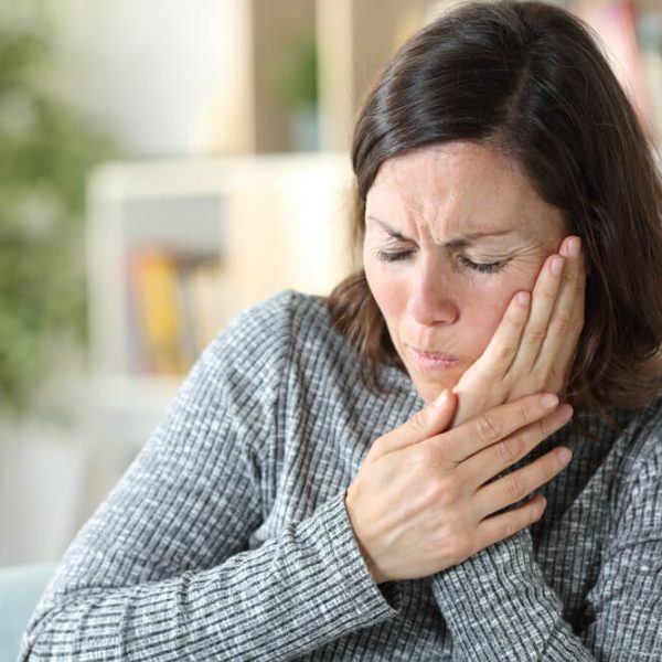 a young woman holding the side of her mouth and wincing in pain