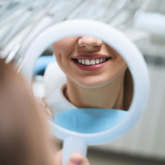 a young woman looking at her new smile in a round handheld mirror