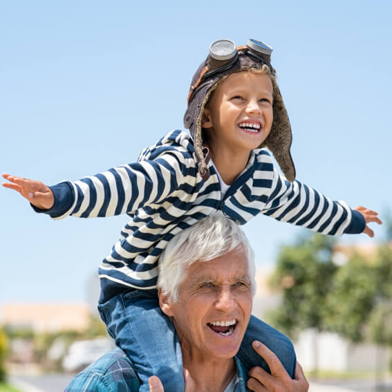 a child on top of an older mans shoulders outside, both smiling