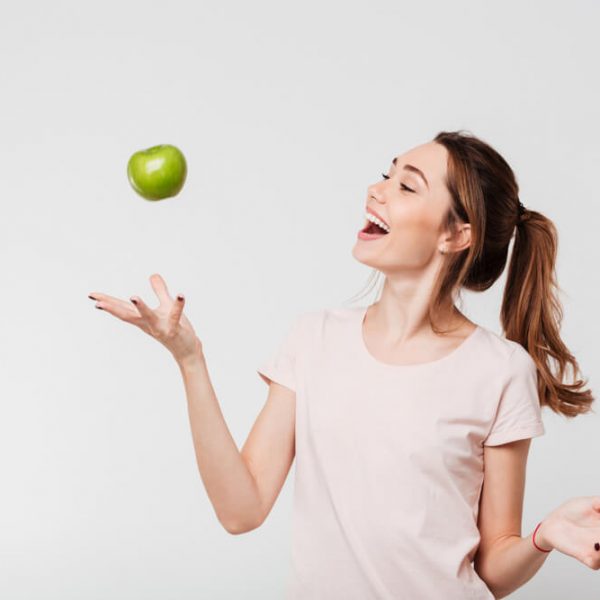 a young woman laughing while tossing up a green apple